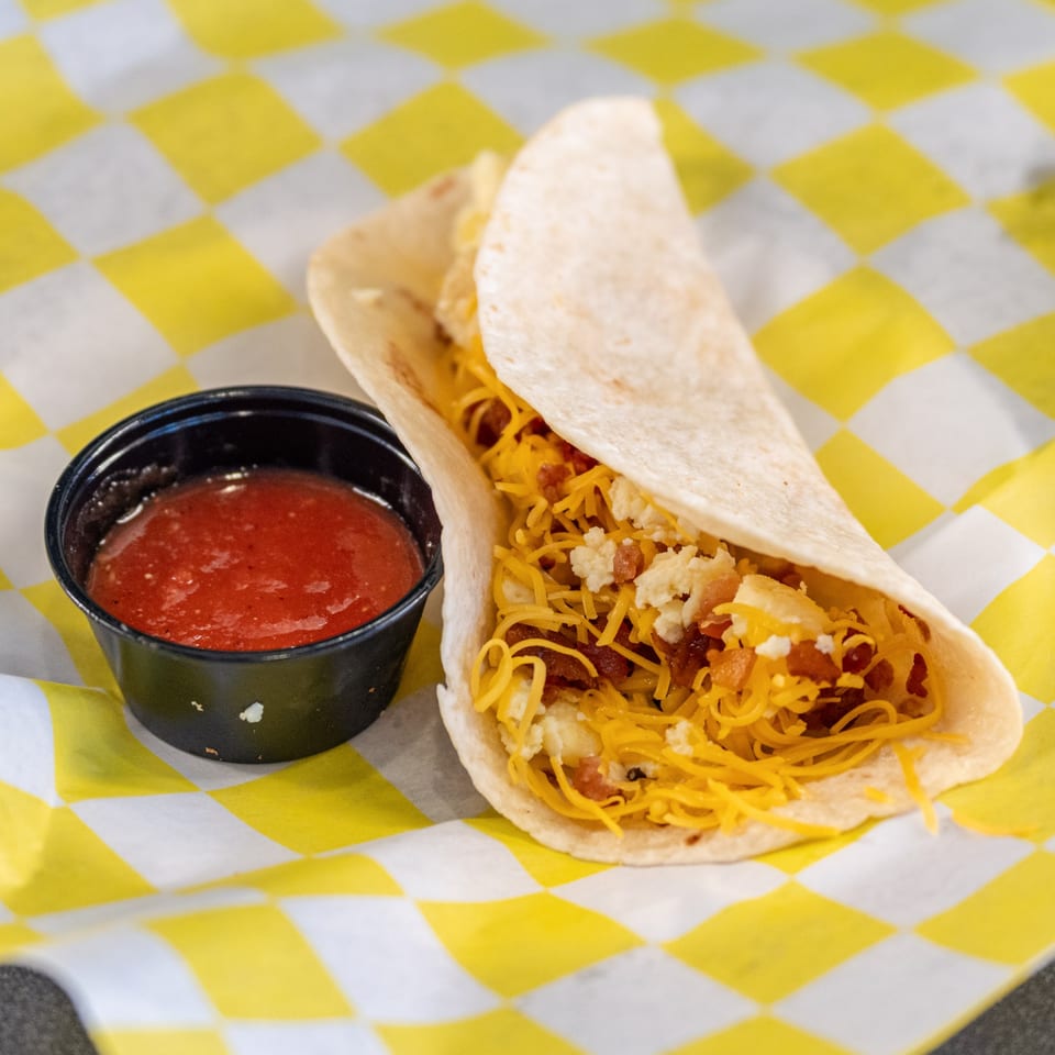 Casa del Taco breakfast taco with scrambled eggs, bacon, and cheese, served with salsa.