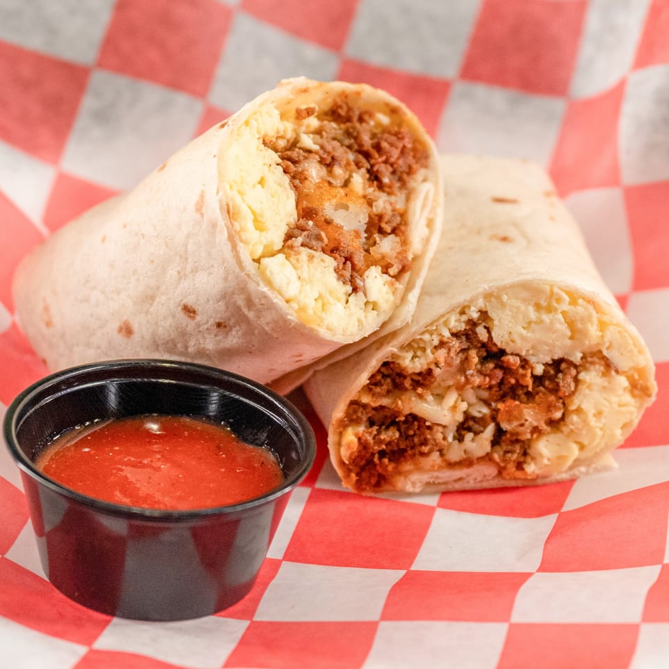Two halves of a breakfast burrito with eggs, meat, and cheese, next to a cup of salsa.