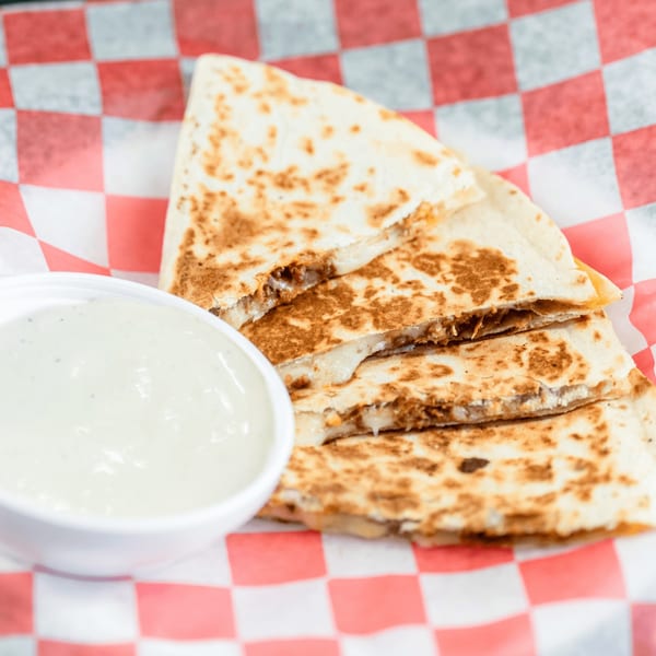 Four quesadilla slices with melted cheese and meat, served with a side of white dipping sauce.