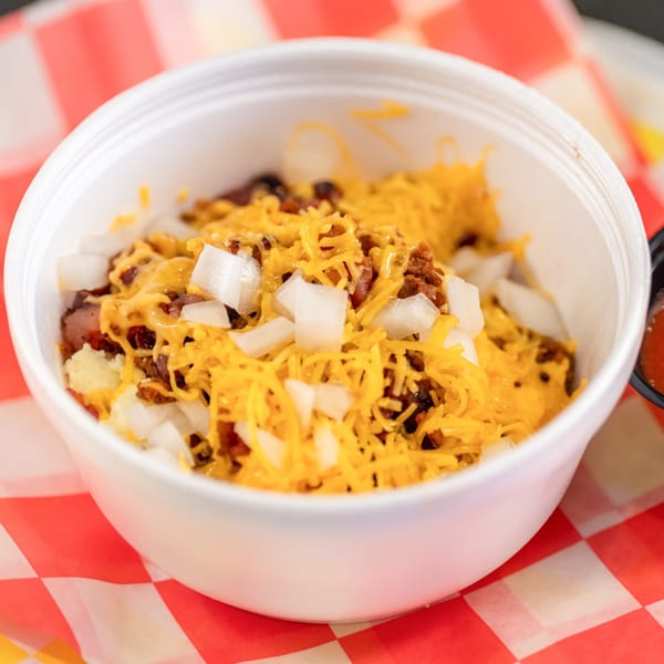 A white bowl of Casa del Taco's chili, cheese, and diced onions on a red and white checkered paper.