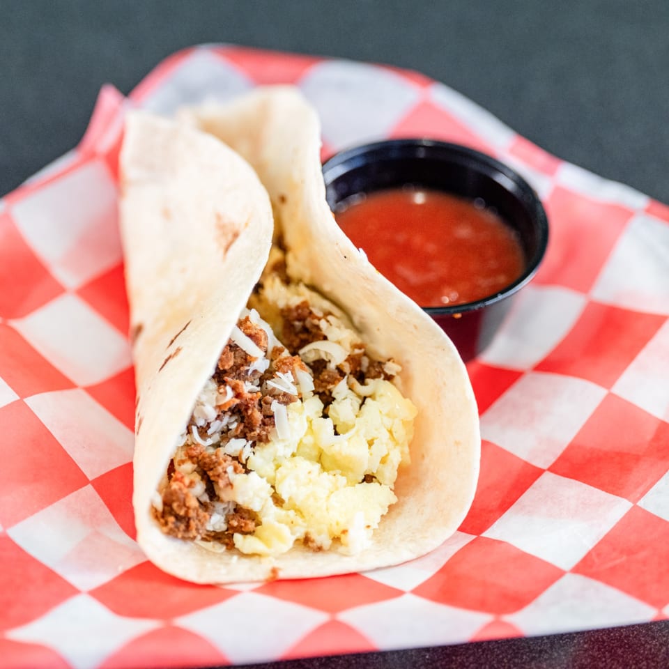 A Casa del Taco breakfast taco with scrambled eggs, chorizo, and cheese, served with salsa.