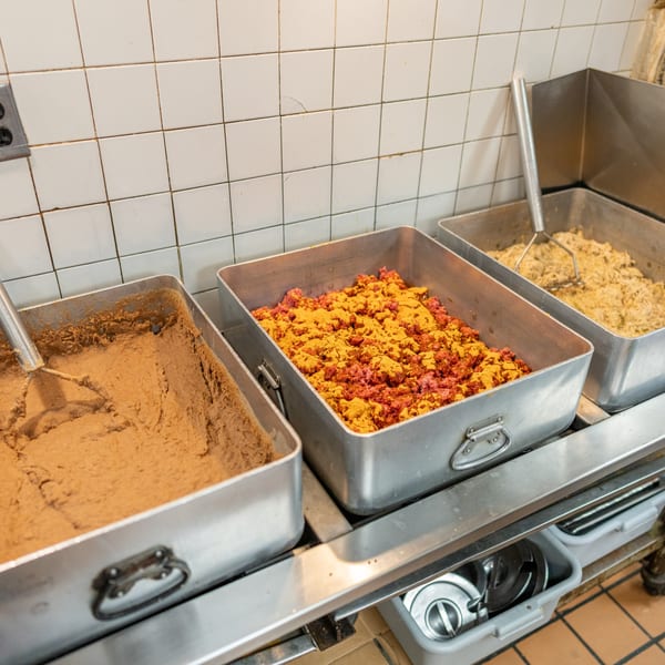 Three metal trays filled with taco ingredients: refried beans, seasoned ground beef, and shredded chicken.