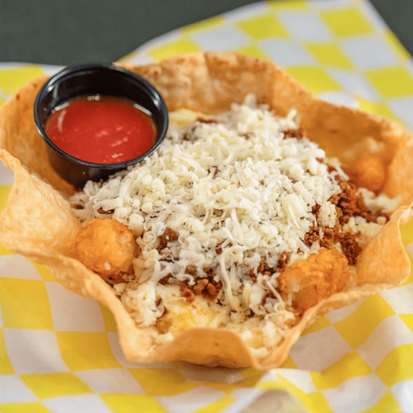 A taco salad in a crispy tortilla bowl, topped with ground meat, shredded cheese, and a side of salsa.