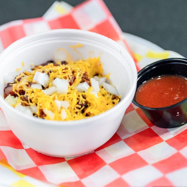 A white bowl of Casa del Taco's chili with cheese and onions, next to a cup of salsa.