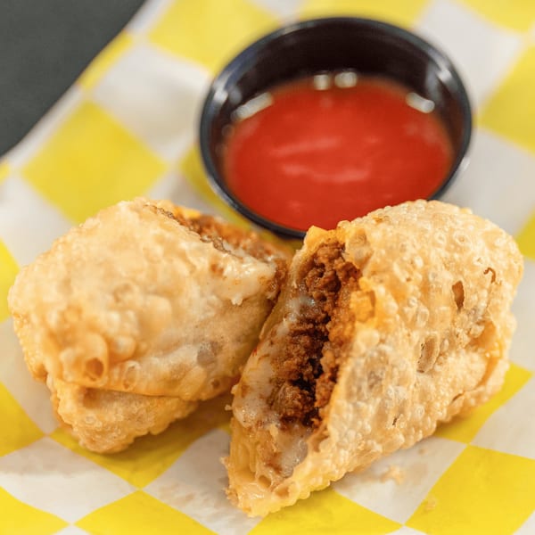 Two crispy, deep-fried tacos filled with ground meat and cheese, served with a side of red sauce.